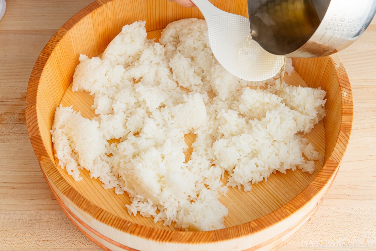 Adding sushi vinegar (sushi rice seasoning) to the cooked rice.
